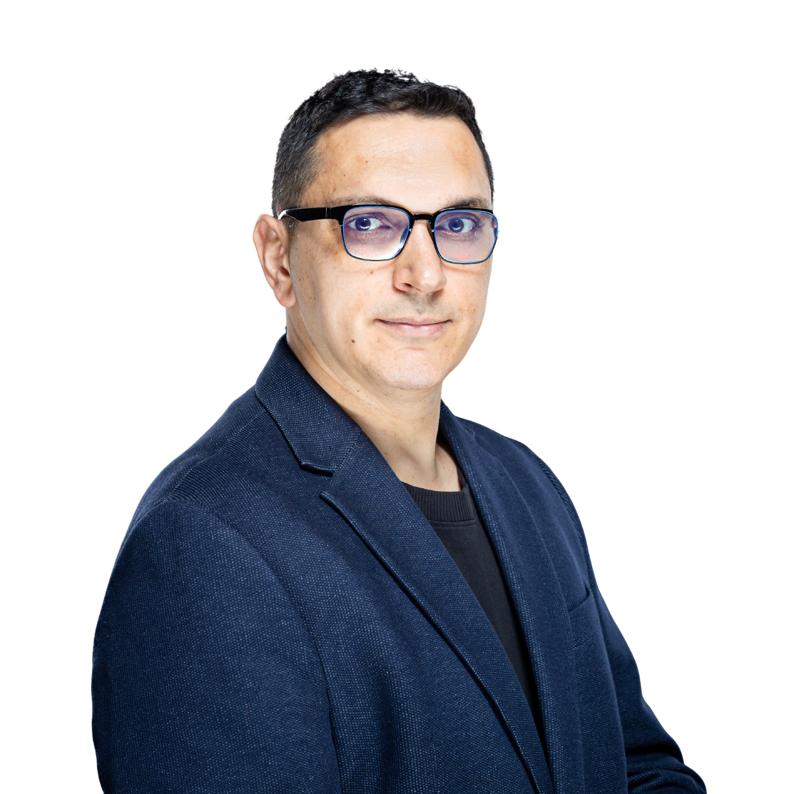 Man with short dark hair and glasses wearing a navy blazer and black shirt, standing in front of a plain white background.
